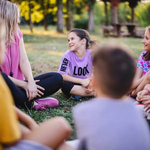 Children sit in a circle on the grass with the teacher and talk after sports activities