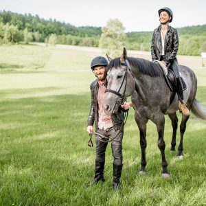 Man leading a horse with woman rider on the beautiful green meadow during the sunny weather