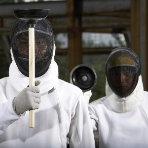 Chinese men in fencing suits with plungers in a construction site