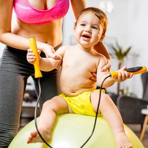 Portrait of a playful baby boy with a rope sitting on the fitball with mother at home